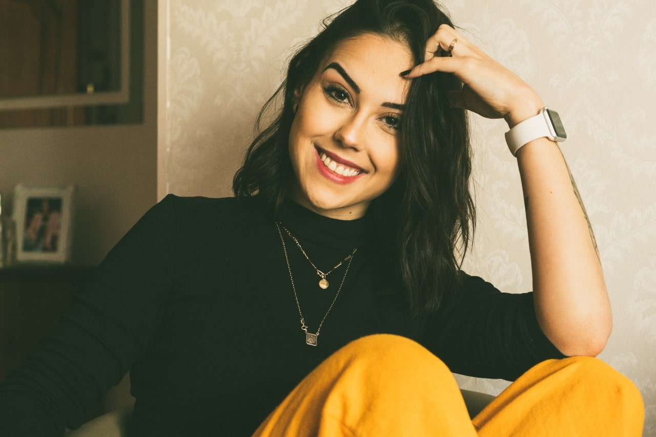 A woman smiling and wearing multiple necklaces and a stylish watch and ring.