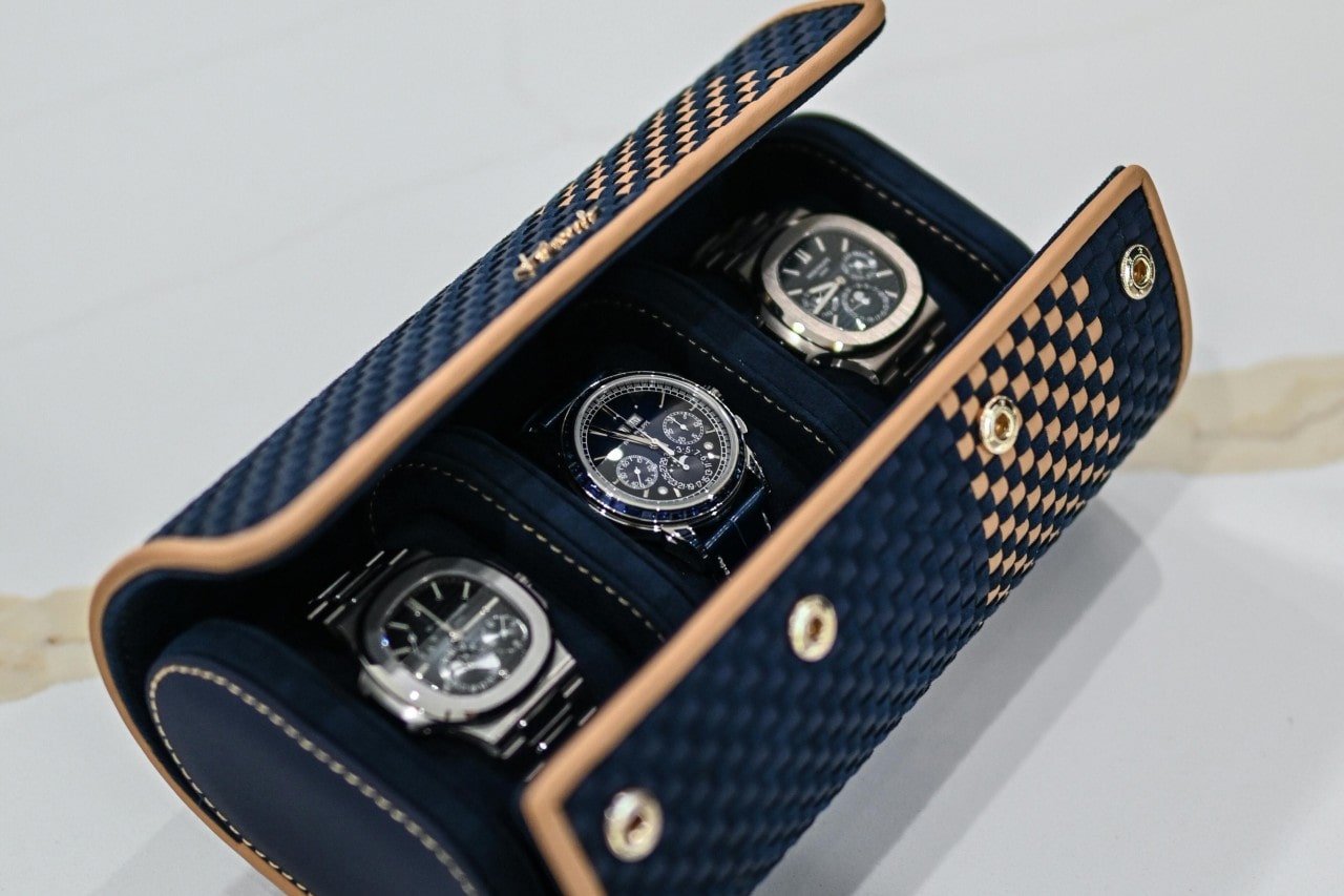 A close-up of three luxury watches displayed side-by-side in a folding leather case.
