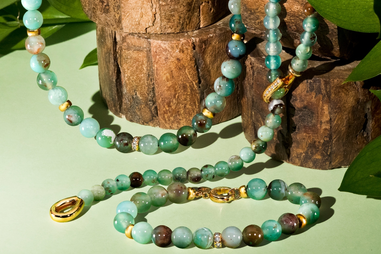 PeacockAquaprase™ necklaces and bracelet sitting on a green background with some tree stumps and leaves