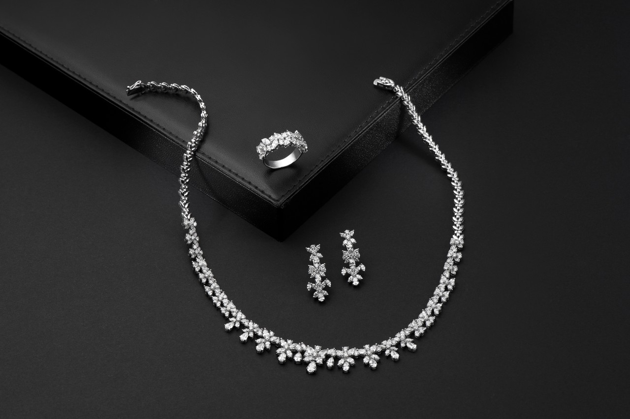 Elegant white gold jewelry set featuring a diamond necklace, matching earrings, and a ring set on black background.