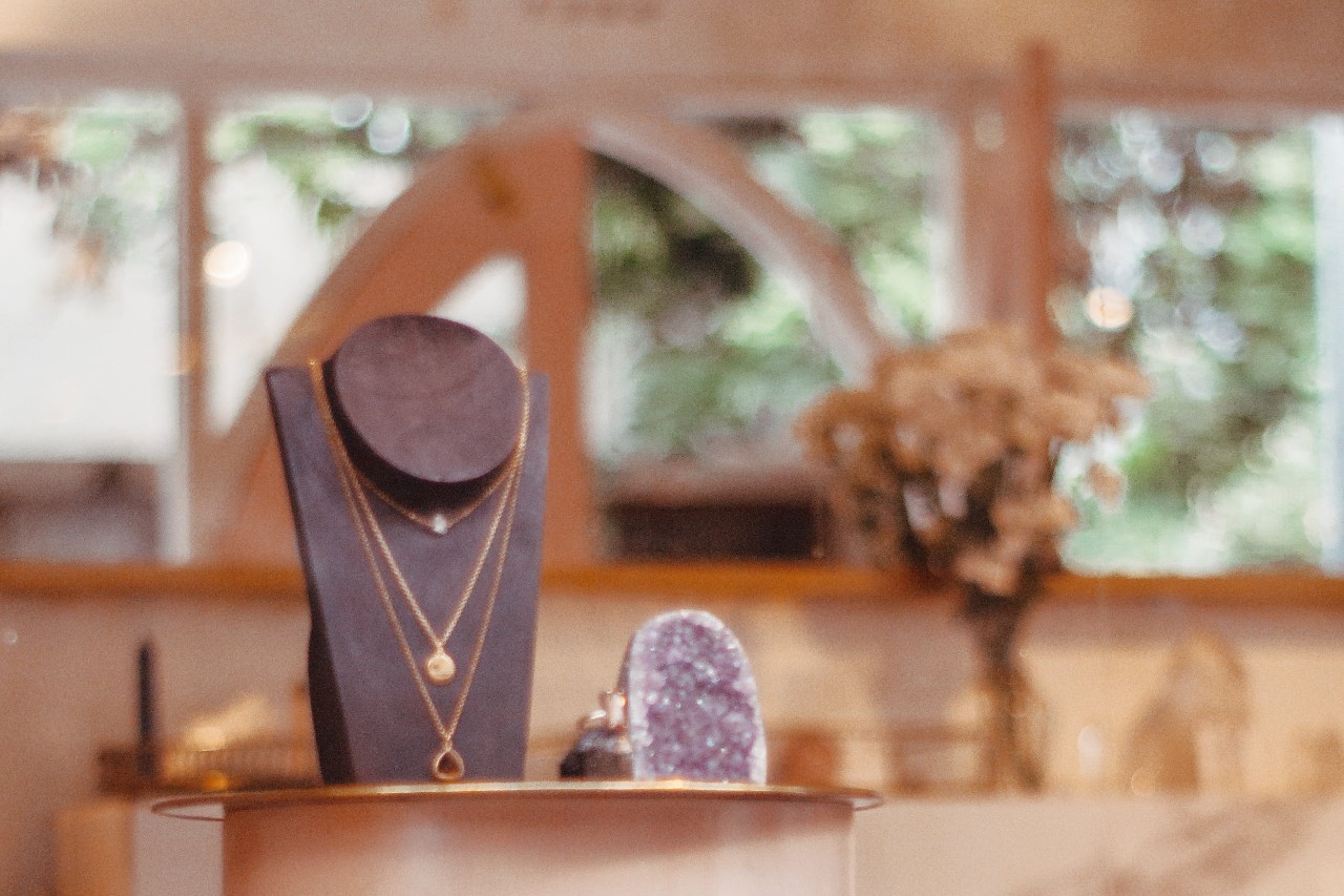 An elegant display of layered gold necklaces on a black velvet stand displayed next to a spectacular purple geode.