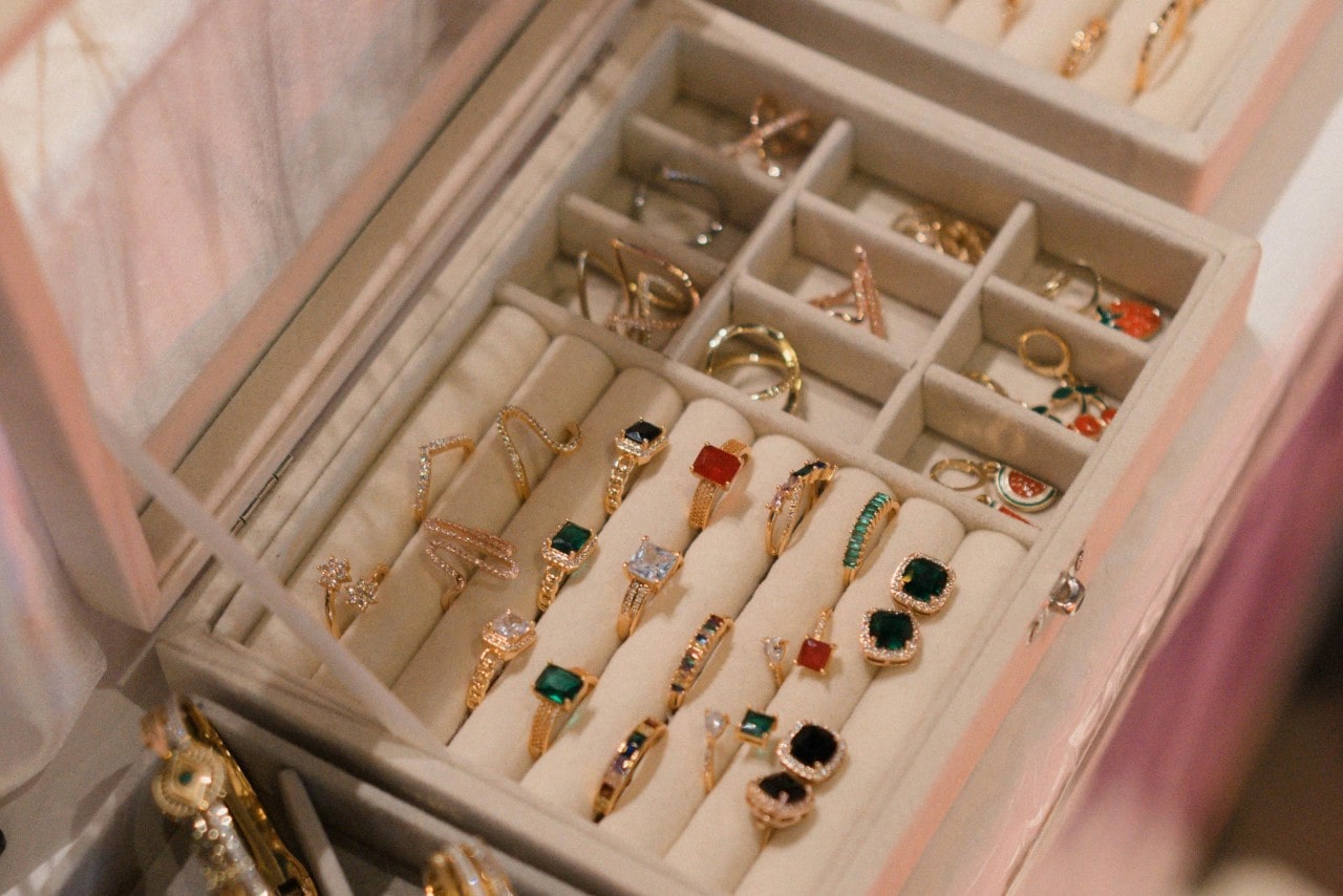A view of an open jewelry box displaying gold rings adorned with various gemstones such as rubies, diamonds, and emeralds.