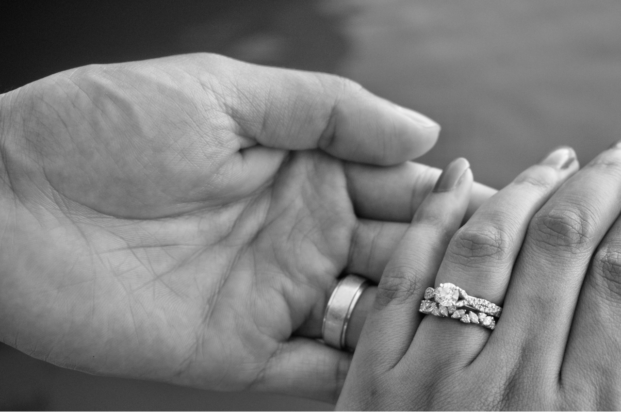 A close-up black-and-white image of the couple's hands, flaunting wedding bands and engagement ring.
