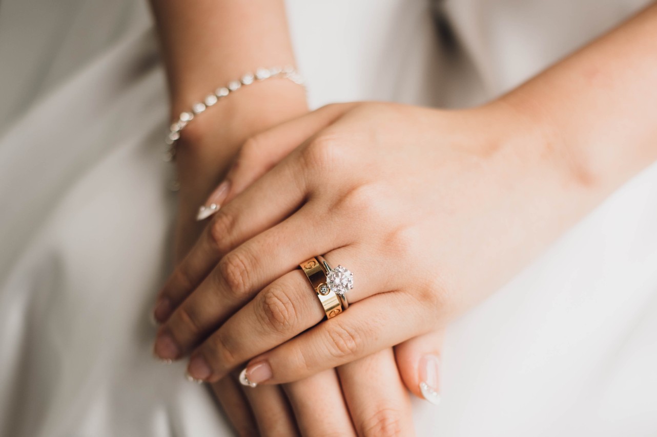 Close-up of a bride's hands with manicured nails, wearing a sparkling diamond ring and gold wedding band.