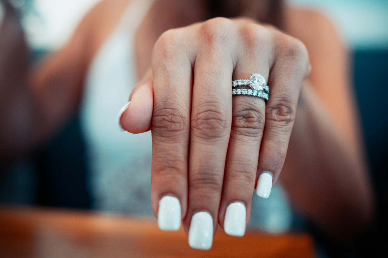 a woman’s extended hand, adorned with a platinum engagement ring and wedding band