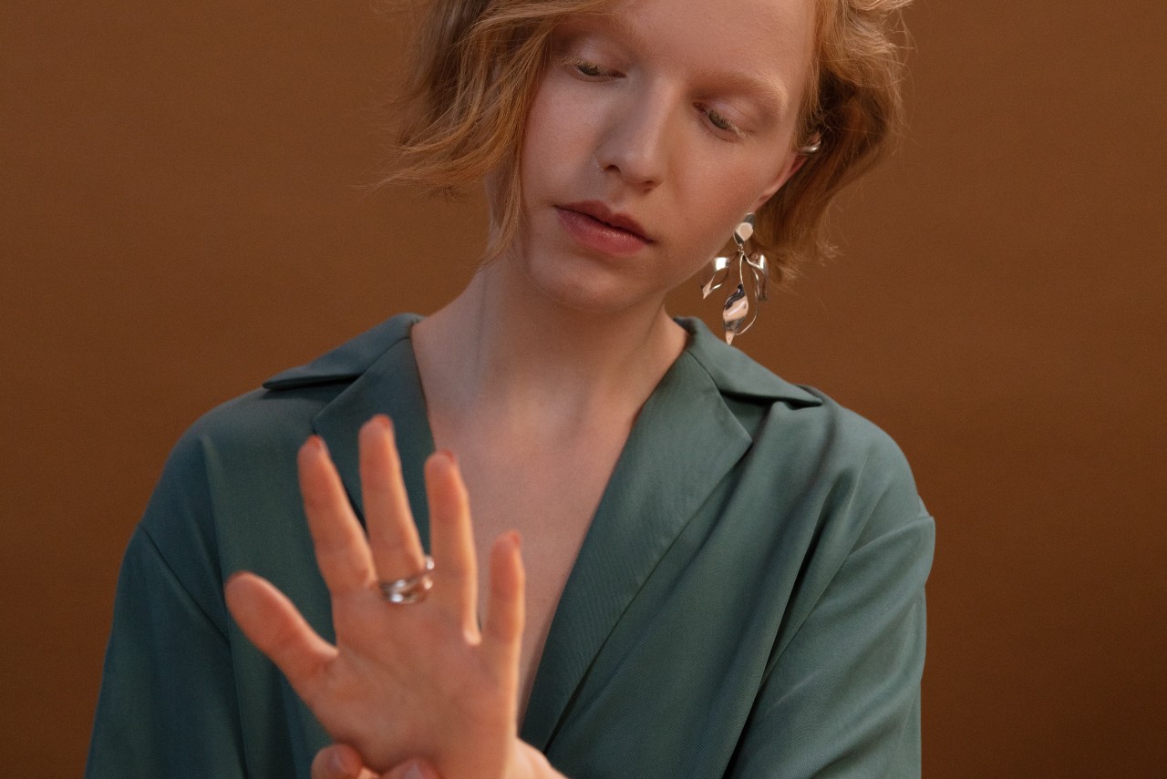 A young woman in a green blouse admires a silver ring on her hand, with her gaze focused on it