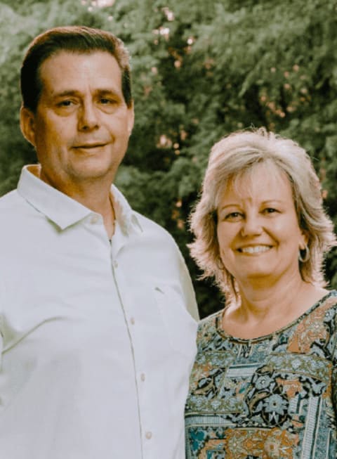 Two people are standing next to each other with a forest in the background