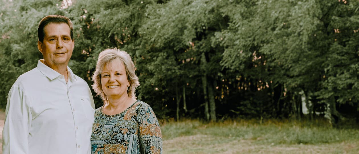 Two people are standing next to each other with a forest in the background