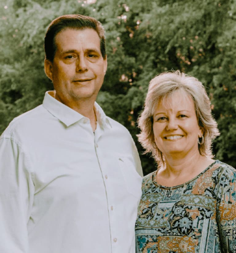 Two people are standing next to each other with a forest in the background