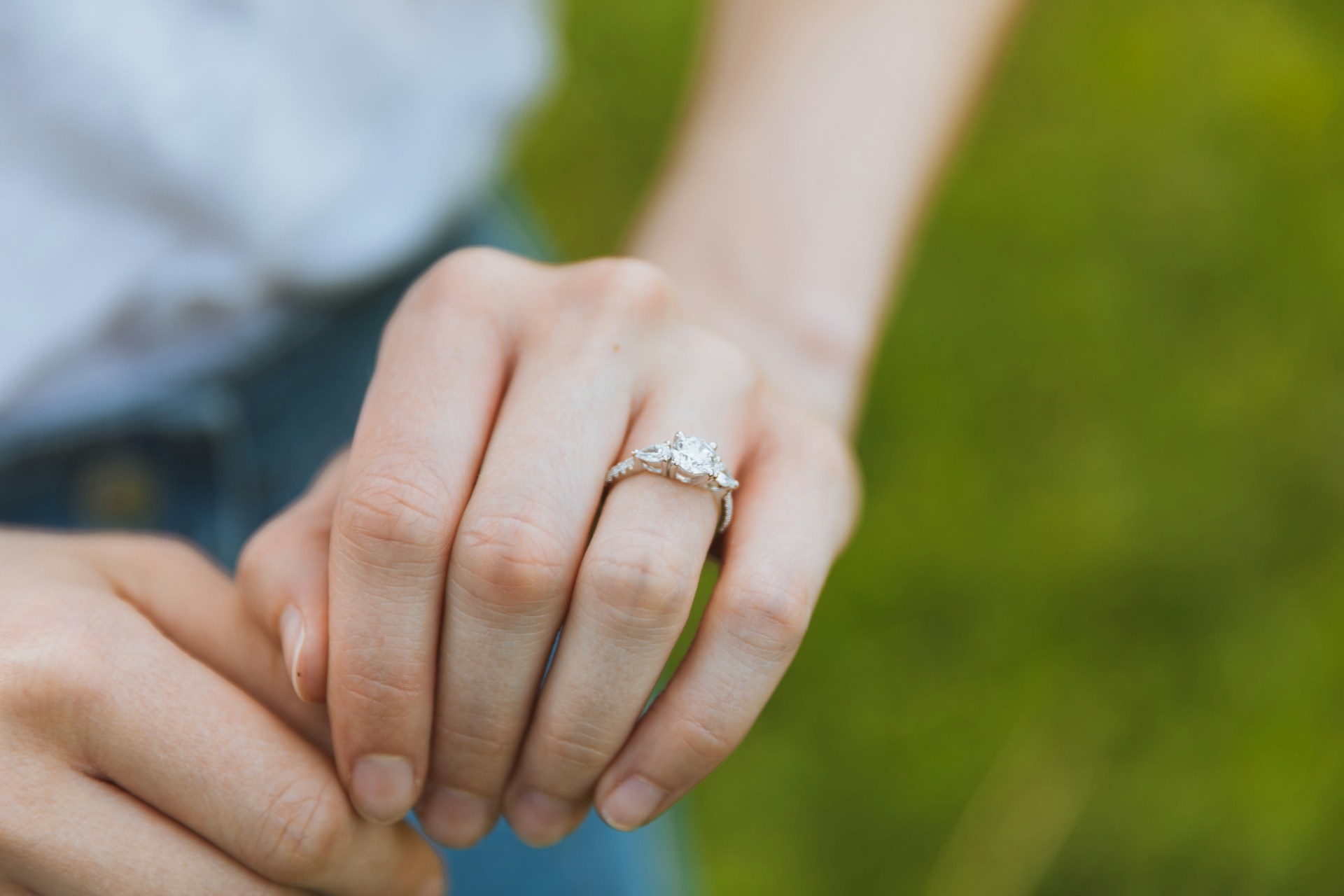 A woman wearing a white gold three stone engagement ring in a grassy field.