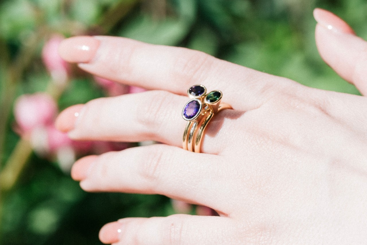an outstretched woman’s hand wearing three stacked gemstone rings an outstretched woman’s hand wearing three stacked gemstone rings
