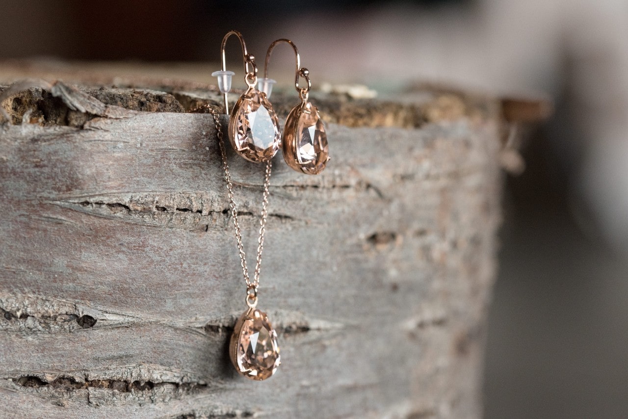 A rose gold set of dangly earrings and a necklace, the jewelry staged on a stump of wood.