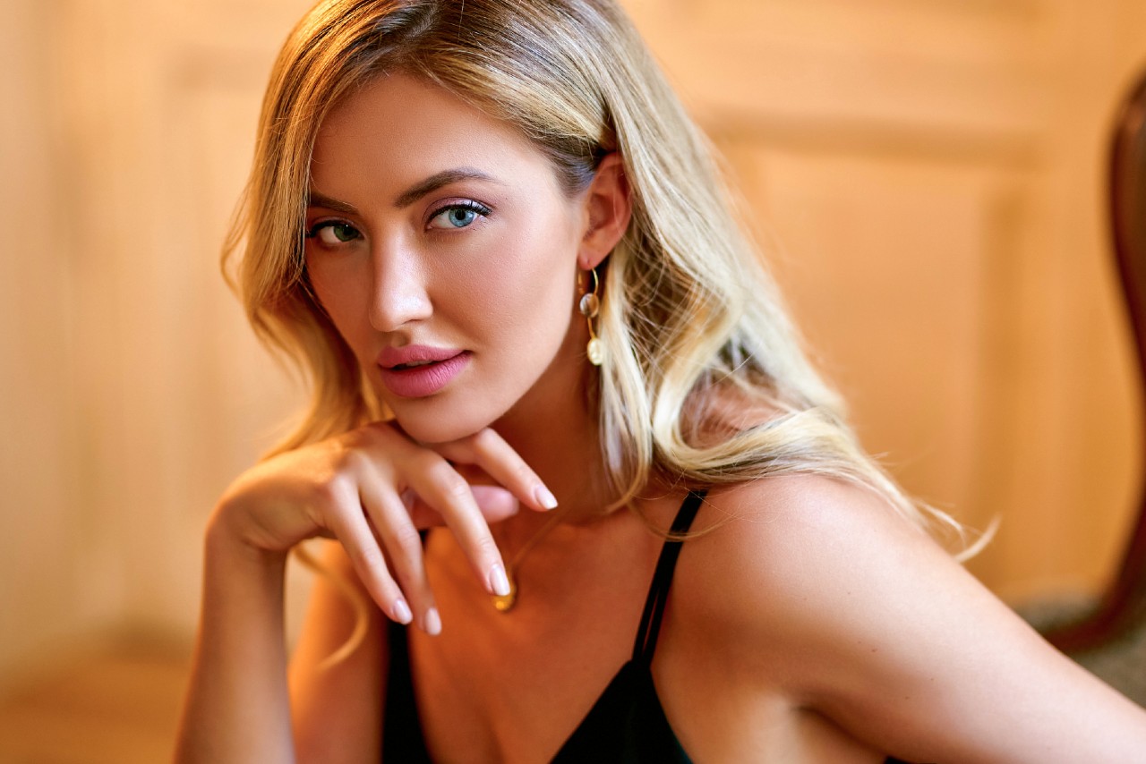 A woman in drop yellow gold earrings with blond hair gazes to the side.