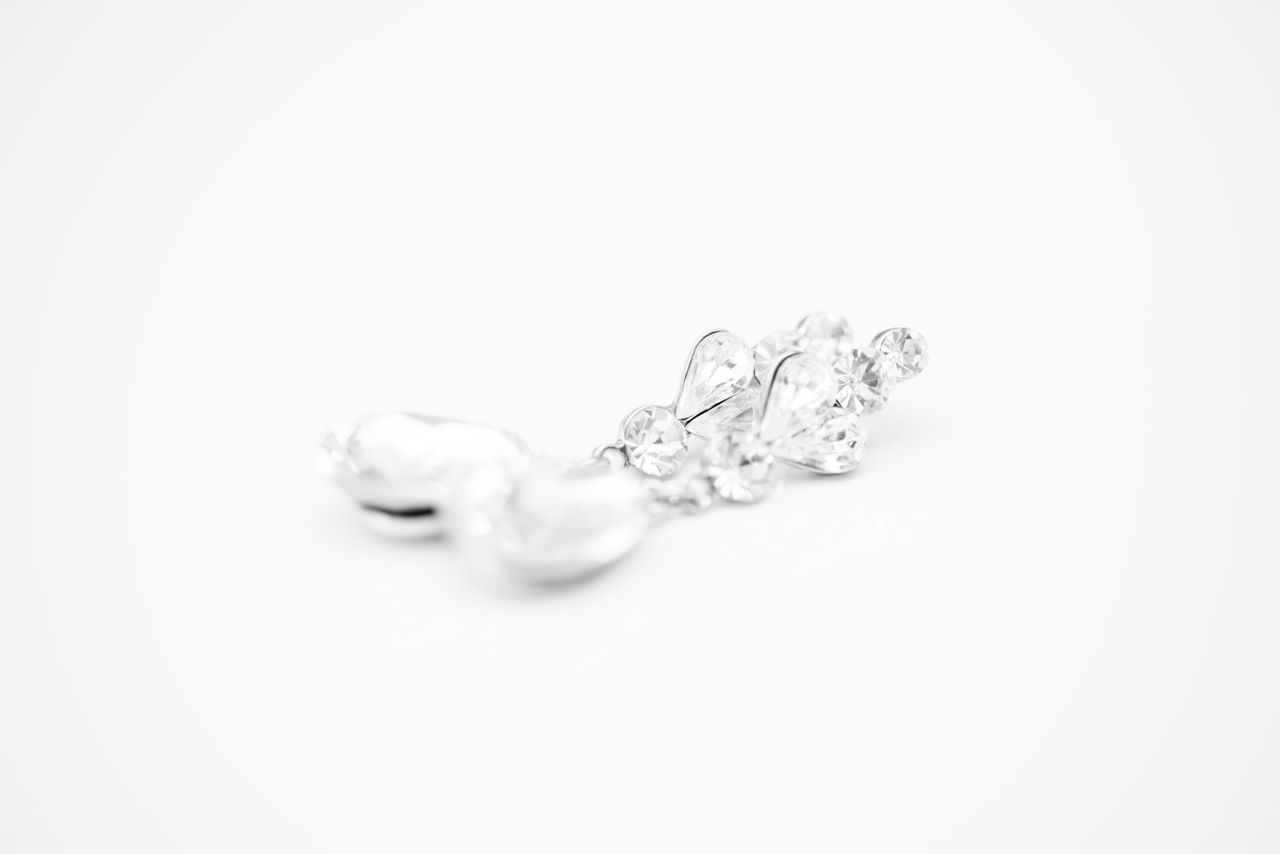A close-up of a pair of pearl and diamond drop earrings on a white surface.