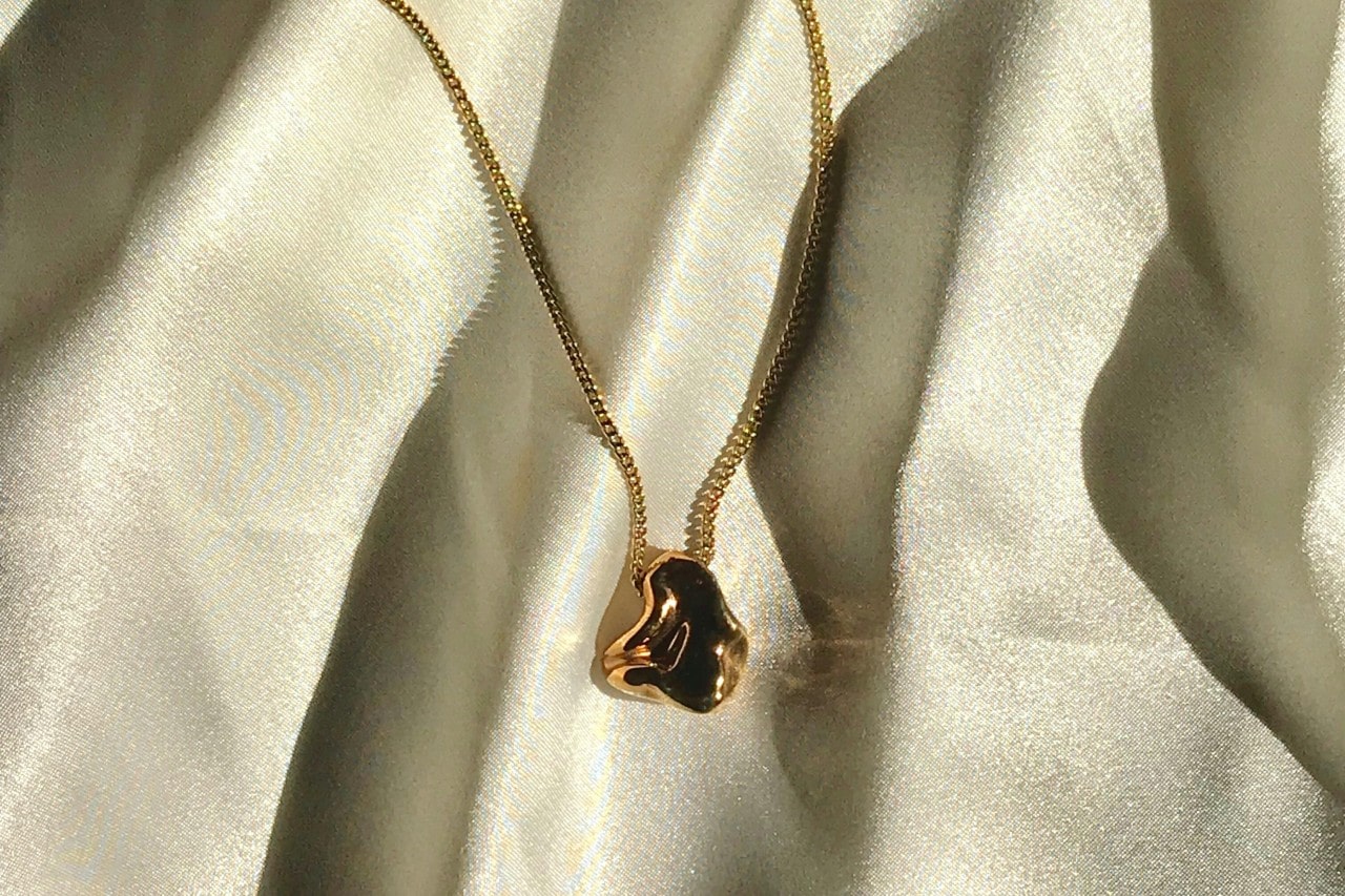 a yellow gold chain necklaces with a sculptural pendant on white fabric a yellow gold chain necklaces with a sculptural pendant on white fabric
