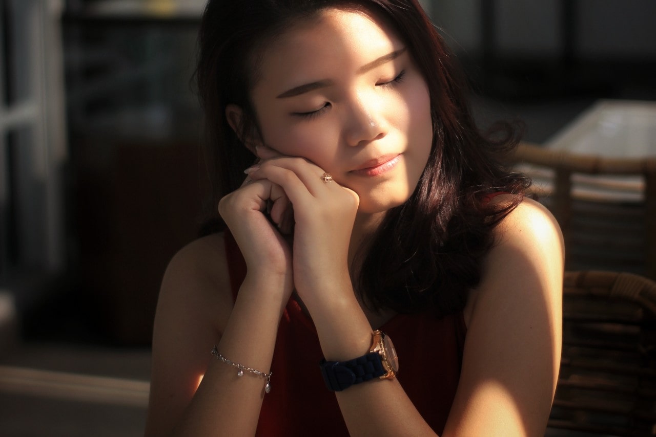 A woman sitting in a restaurant uses her hands to support her head. A woman sitting in a restaurant uses her hands to support her head.