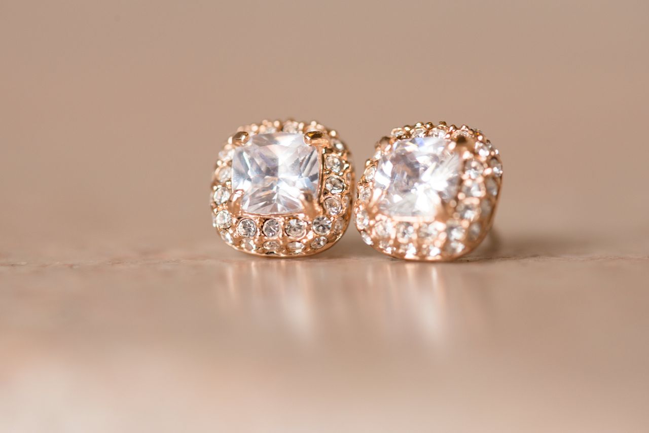 A pair of rose gold earrings adorned with cushion-cut gemstones surrounded by sparkling pavé-set diamonds on a beige background. A pair of rose gold earrings adorned with cushion-cut gemstones surrounded by sparkling pavé-set diamonds on a beige background.