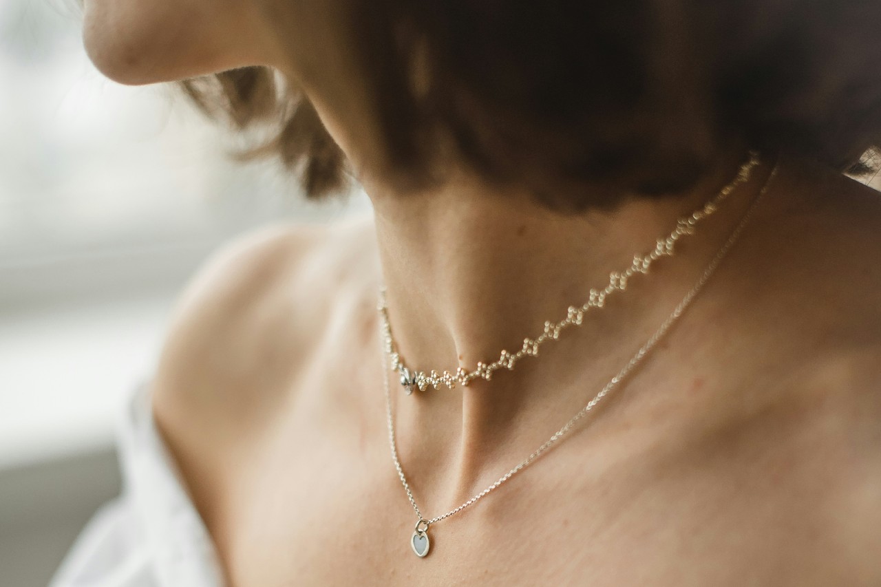 A close-up of a woman's neck adorned with a delicate pearl choker and a fine chain necklace featuring a small, heart-shaped pendant. A close-up of a woman's neck adorned with a delicate pearl choker and a fine chain necklace featuring a small, heart-shaped pendant.