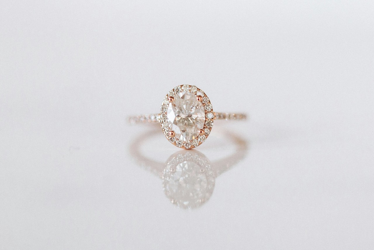 A close-up of a pear cut diamond halo ring with side stones along its rose gold band.
