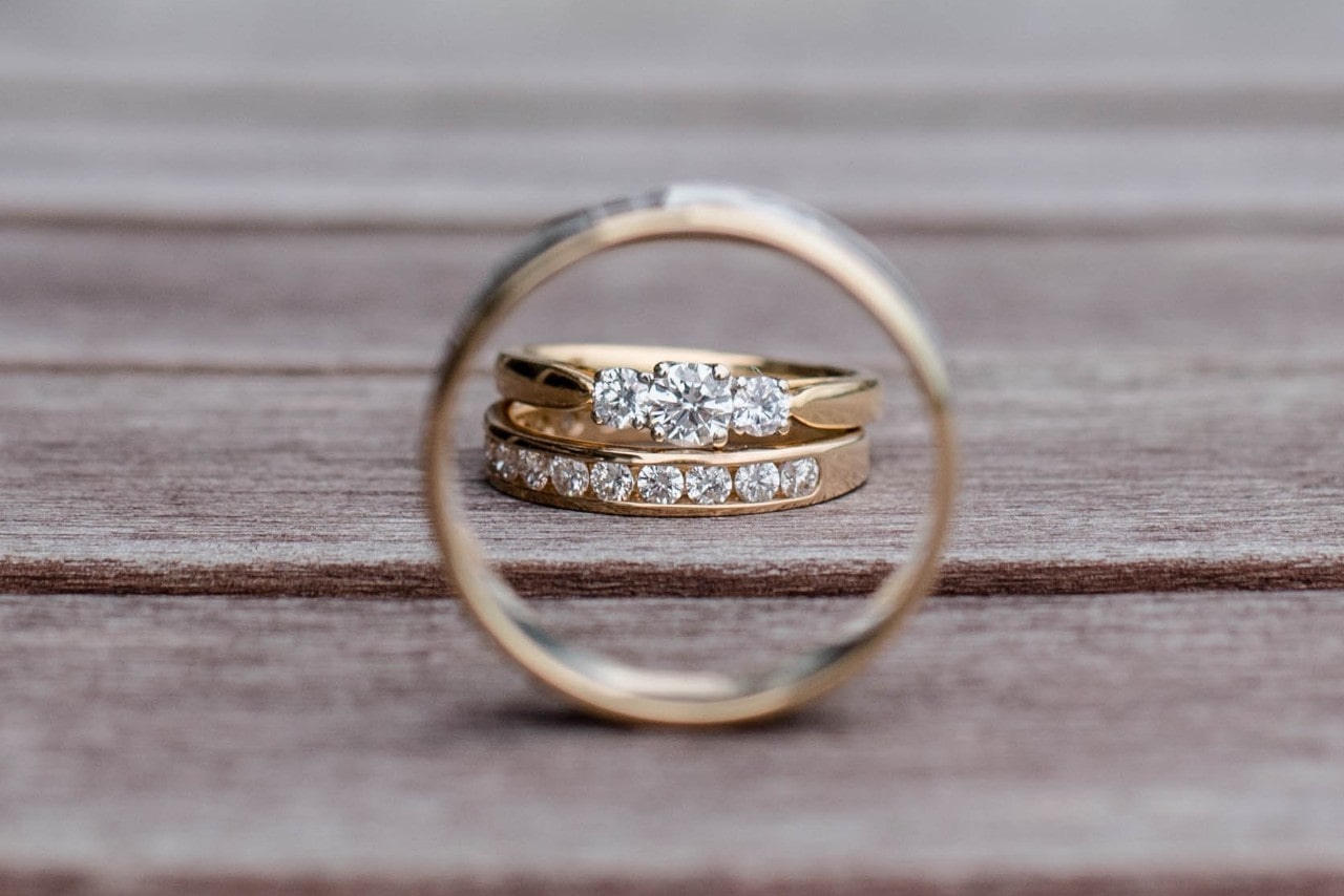 Two diamond-studded gold bands are framed through another ring and rest on a wooden surface.