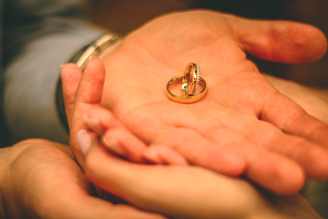 A close up of two yellow gold wedding bands on a man’s palm.