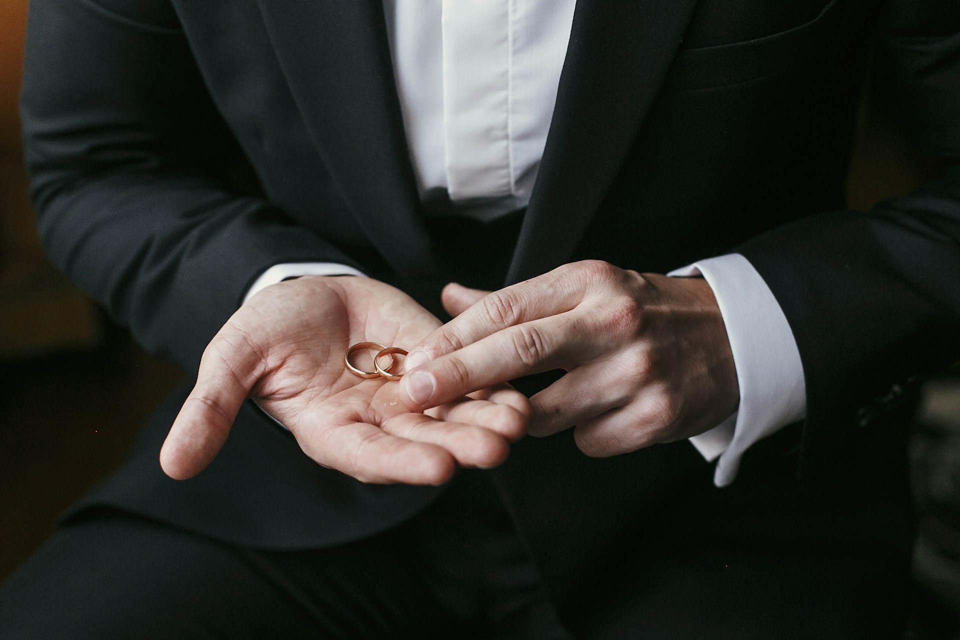 A groom holding matching yellow gold wedding bands in his hand. A groom holding matching yellow gold wedding bands in his hand.