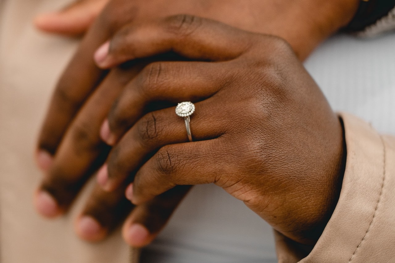 A close-up of a hand wearing a halo engagement ring with a round center stone A close-up of a hand wearing a halo engagement ring with a round center stone