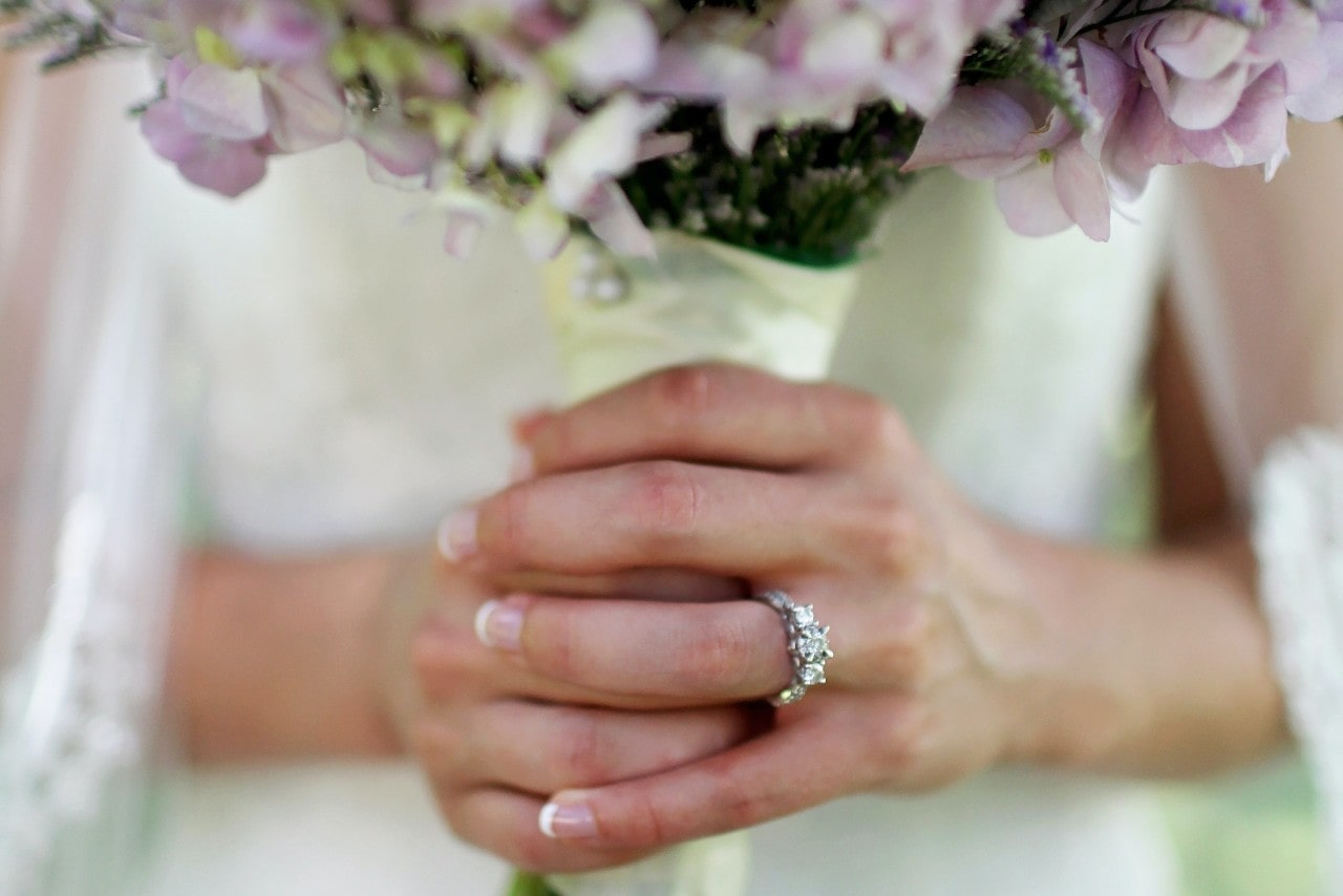 A bride's hands holding a bouquet of pastel flowers, adorned with a sparkling multi-stone engagement ring A bride's hands holding a bouquet of pastel flowers, adorned with a sparkling multi-stone engagement ring