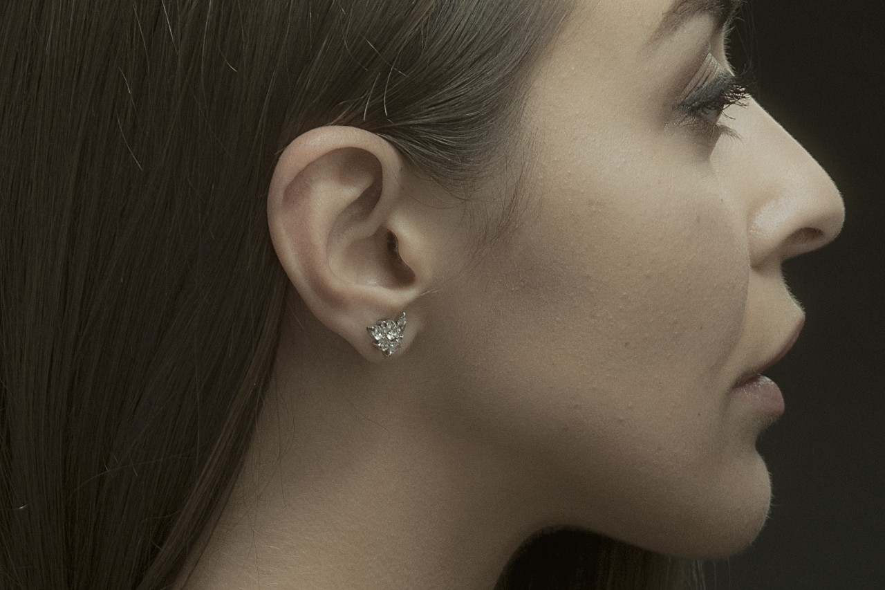 A side profile of a young woman wearing a floral diamond stud earrings.