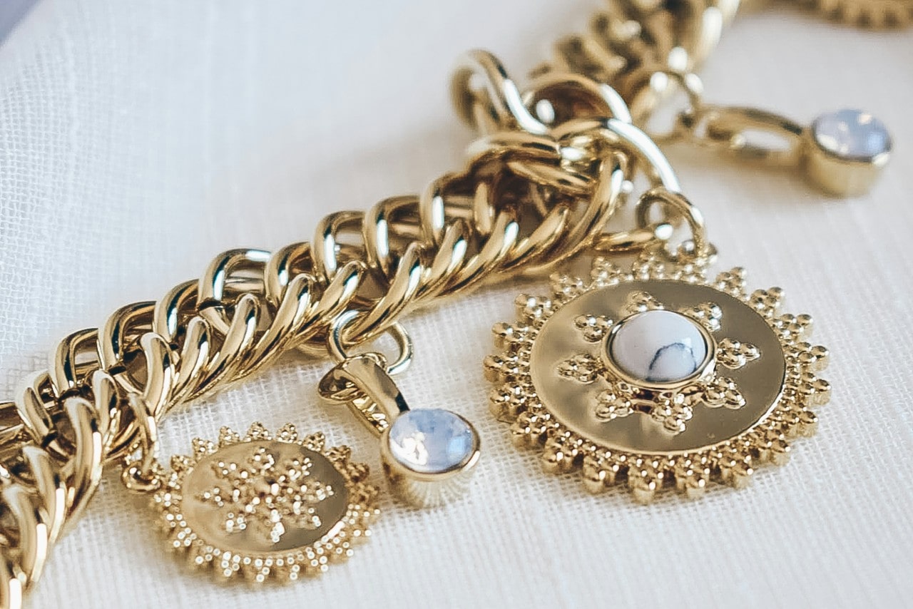 A close-up of a yellow gold chain bracelet with sun motifs and vibrant gemstones.