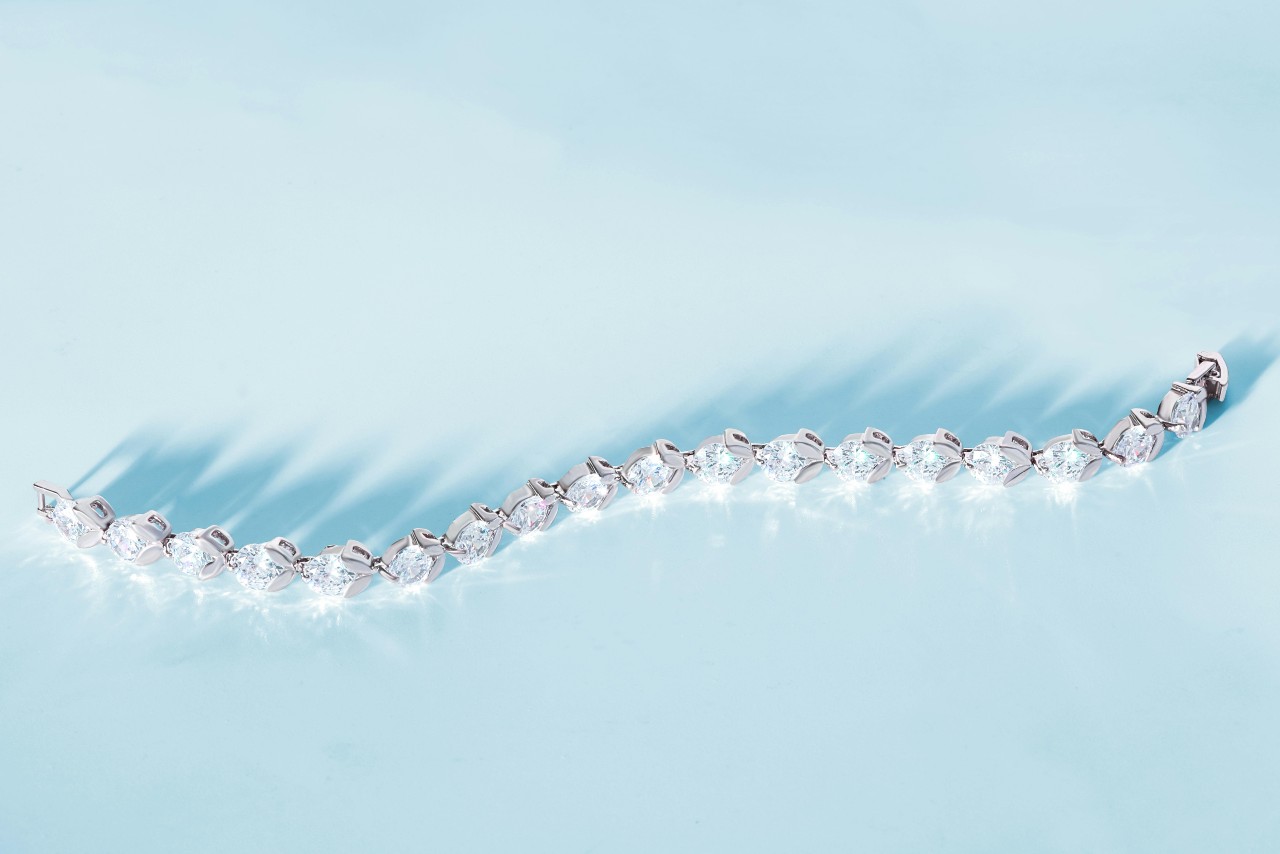 A close-up of a diamond tennis bracelet beautifully refracting light onto a pale blue backdrop. A close-up of a diamond tennis bracelet beautifully refracting light onto a pale blue backdrop.