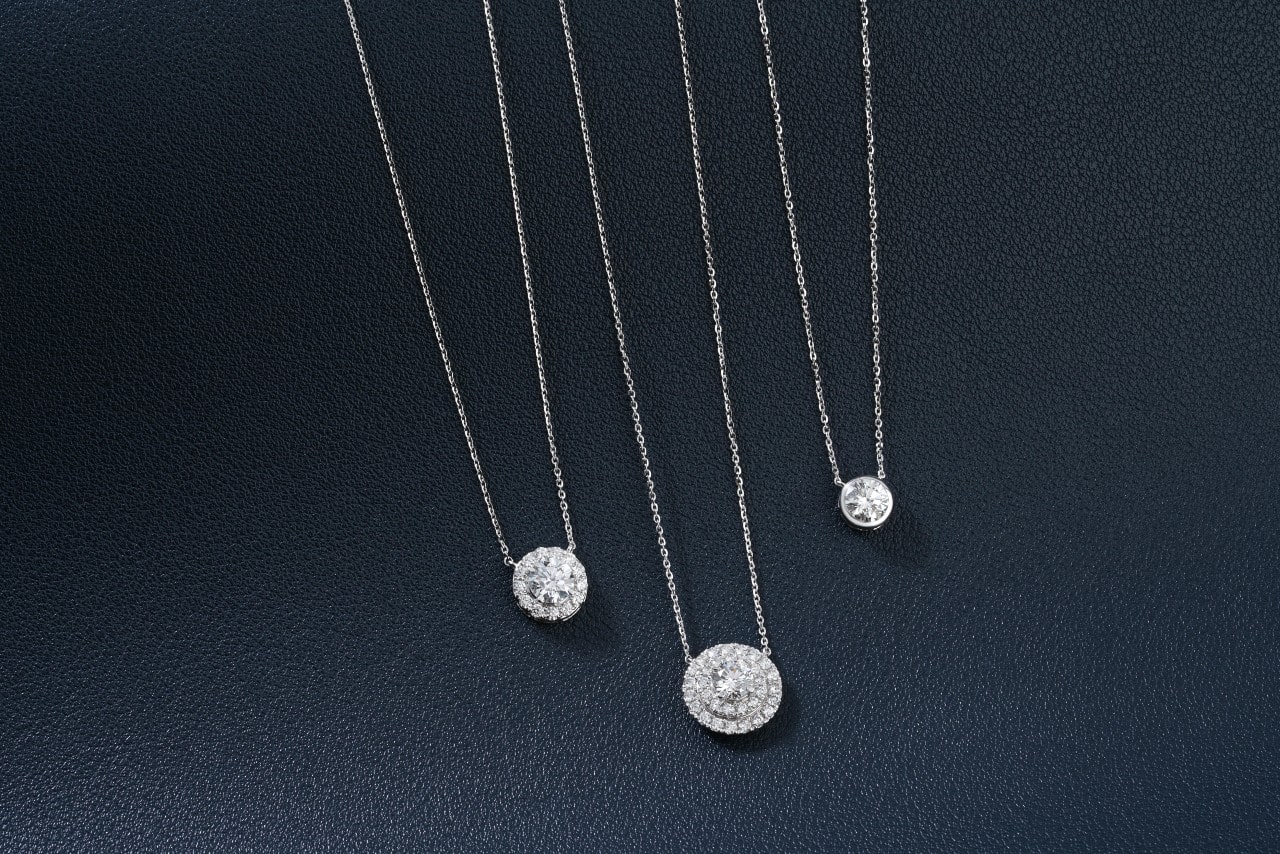 A close-up of three delicate diamond pendant necklaces on a dark, textured backdrop. A close-up of three delicate diamond pendant necklaces on a dark, textured backdrop.