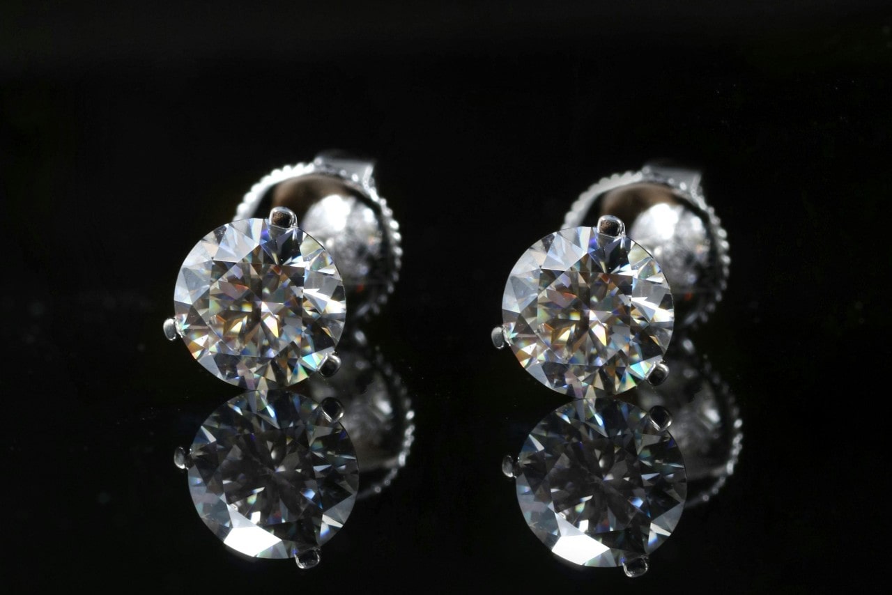 A close-up of a pair of dazzling diamond stud earrings on a dark, reflective backdrop. A close-up of a pair of dazzling diamond stud earrings on a dark, reflective backdrop.