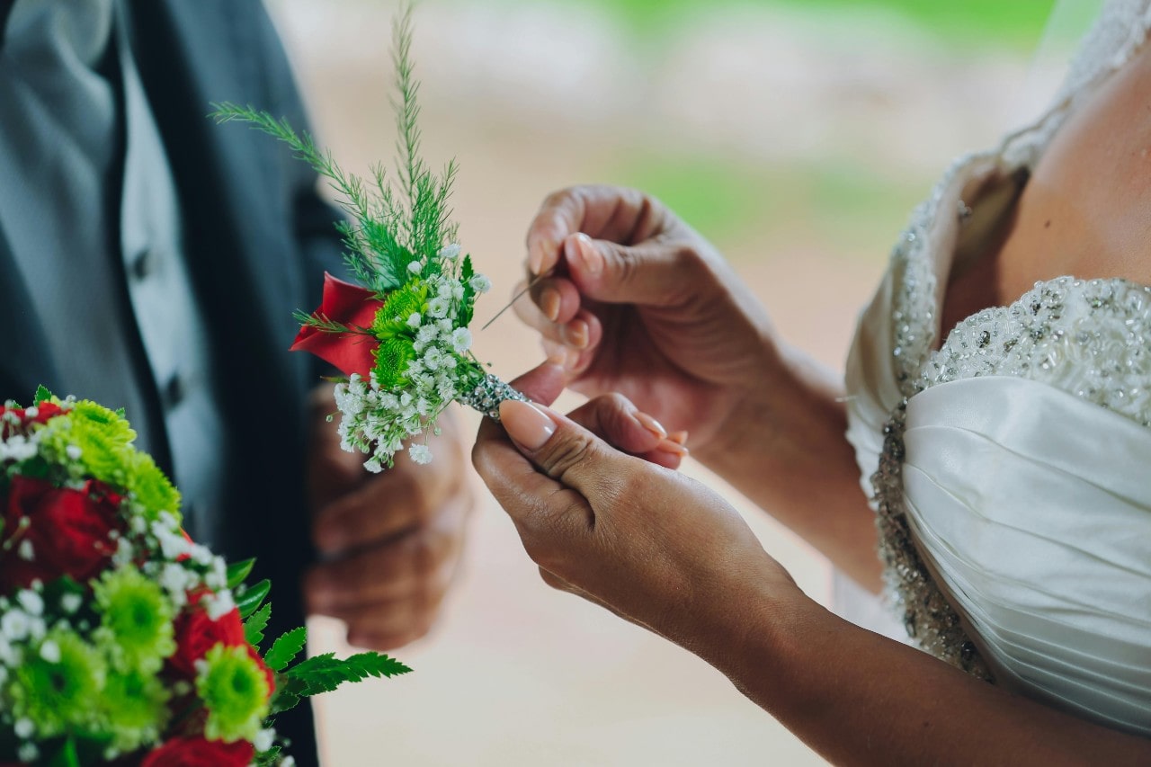 A close-up of a bride preparing to pin a boutonniere on her groom’s suit. A close-up of a bride preparing to pin a boutonniere on her groom’s suit.
