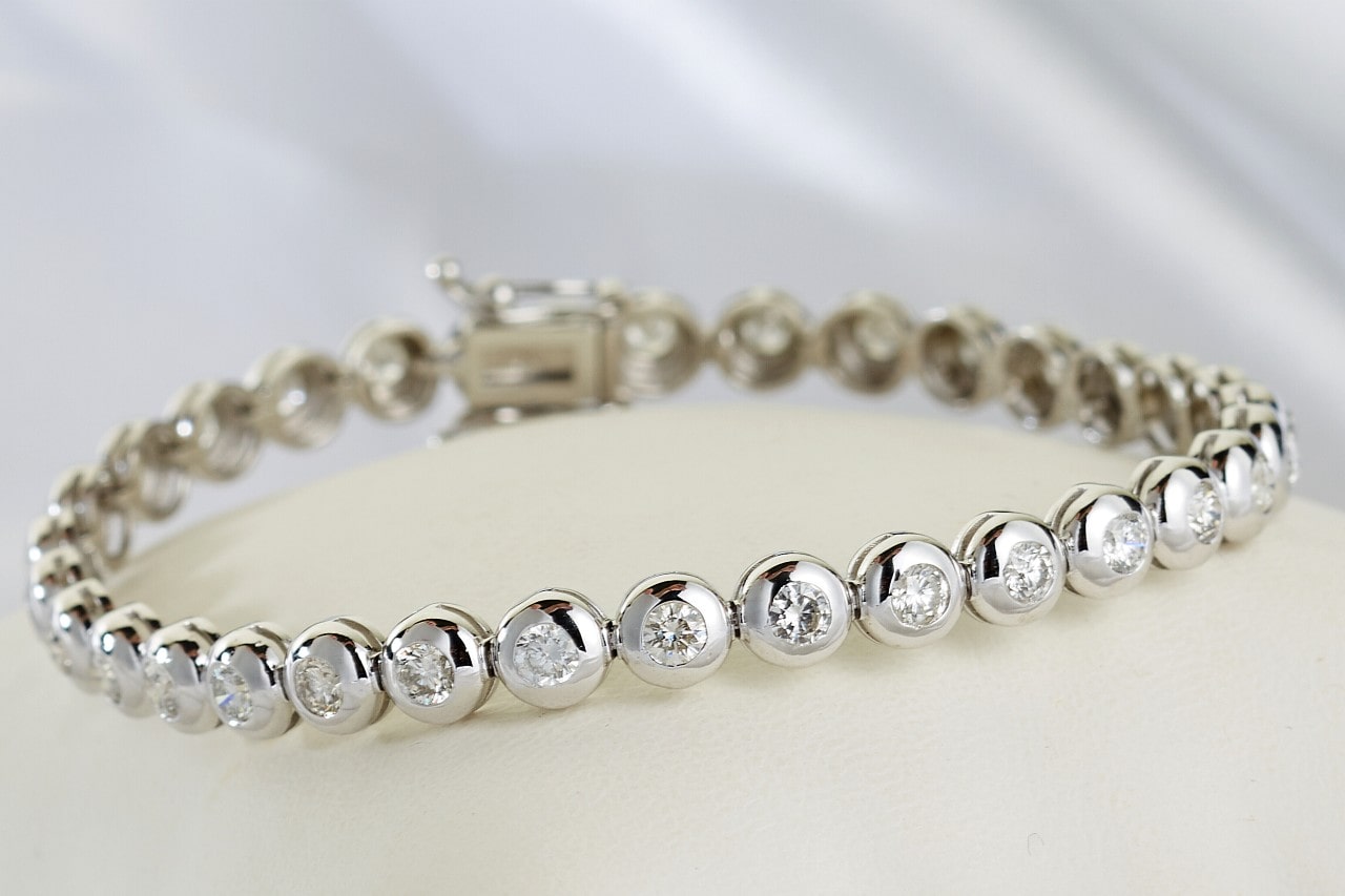 Elegant white gold tennis bracelet adorned with round, sparkling diamonds rests on a soft white cushion.